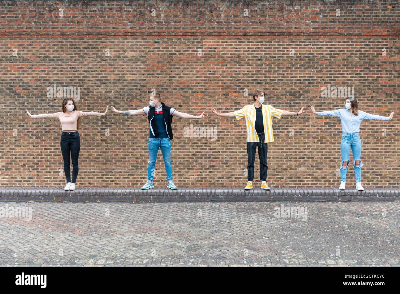 Männliche und weibliche Freunde mit ausgestreckten Armen, die einen sicheren Abstand halten Beim Stehen gegen Ziegelwand Stockfoto