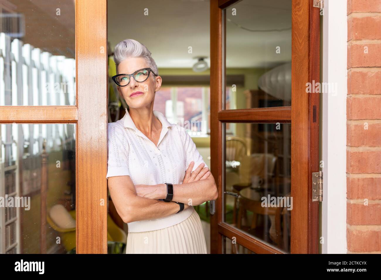 Betrachten ältere Frau mit gekreuzten Armen stehend auf Tür an Zu Hause Stockfoto
