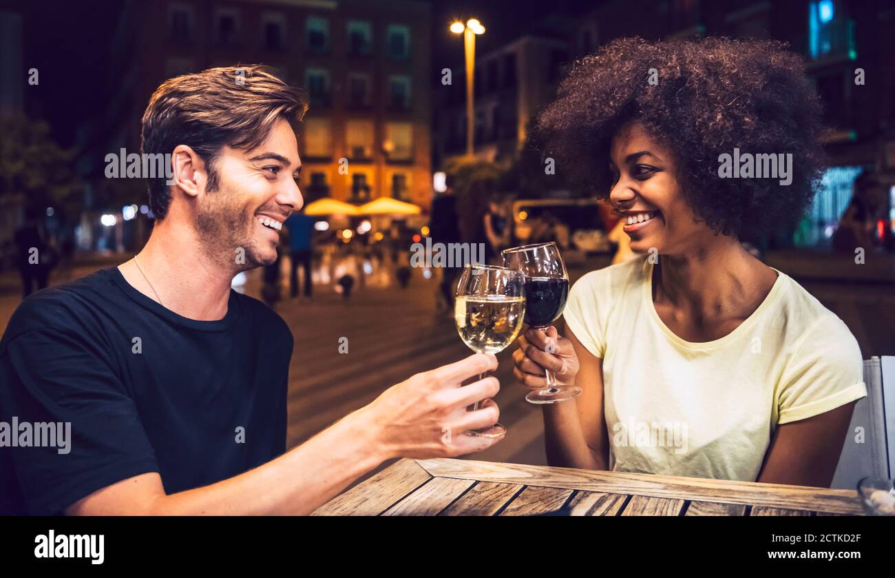 Fröhliches Paar, das sich ansieht, während sie Weingläser anrösten Datum Nacht Stockfoto