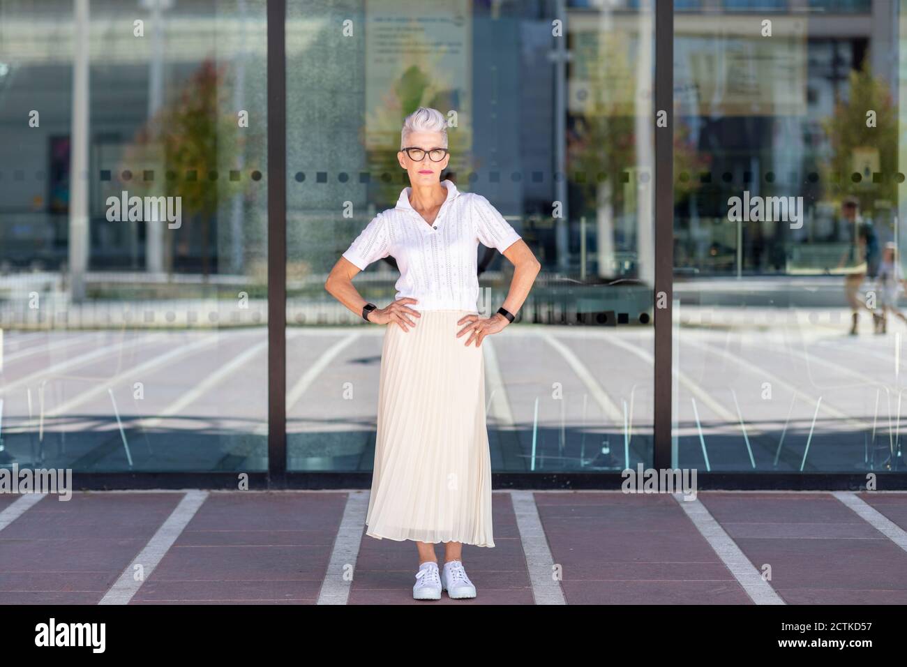Frau mit der Hand auf der Hüfte, die gegen das Glasfenster steht Stadt Stockfoto
