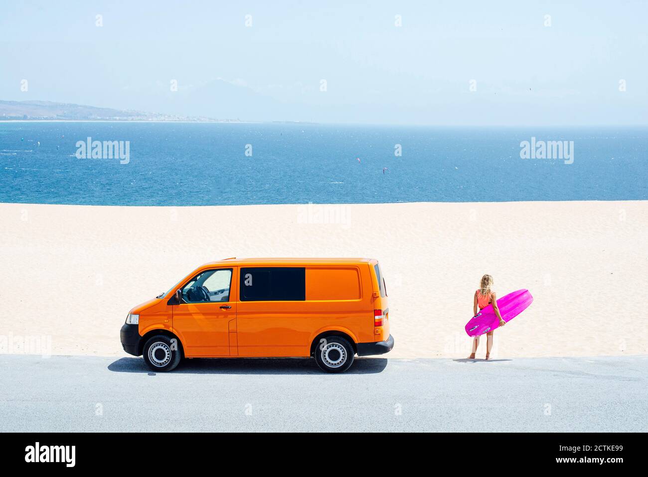 Weibliche Reisende mit Blick auf das Meer, während sie am Strand stehen Surfbrett an sonnigen Tagen Stockfoto