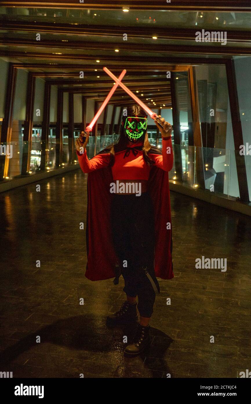 Grüne Neon-Maskenfigur, mit roten Lichtschwert im Umhang, im dunklen Eingang, dezente Beleuchtung Stockfoto