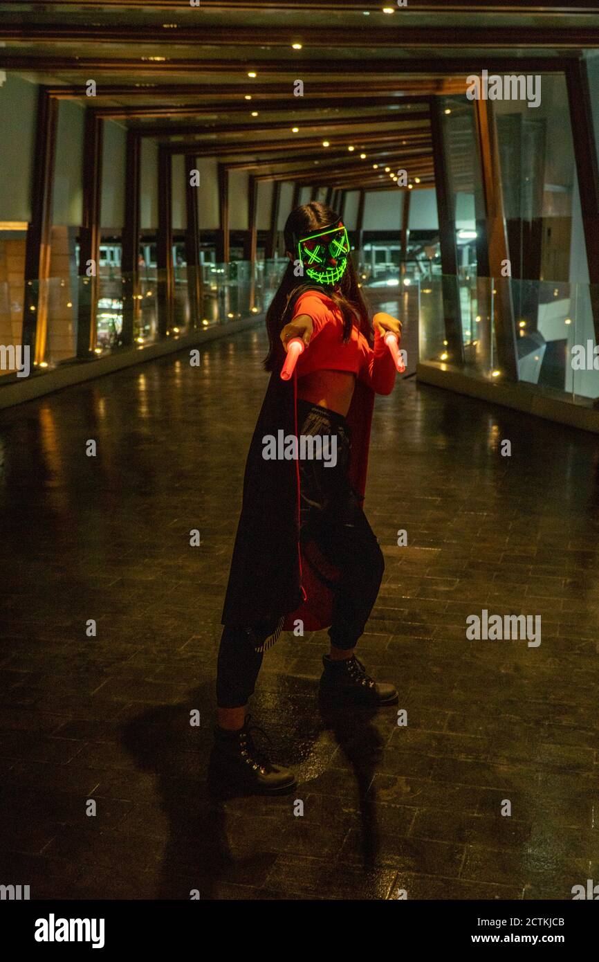 Grüne Neon-Maskenfigur, mit roten Lichtschwert im Umhang, im dunklen Eingang, dezente Beleuchtung Stockfoto