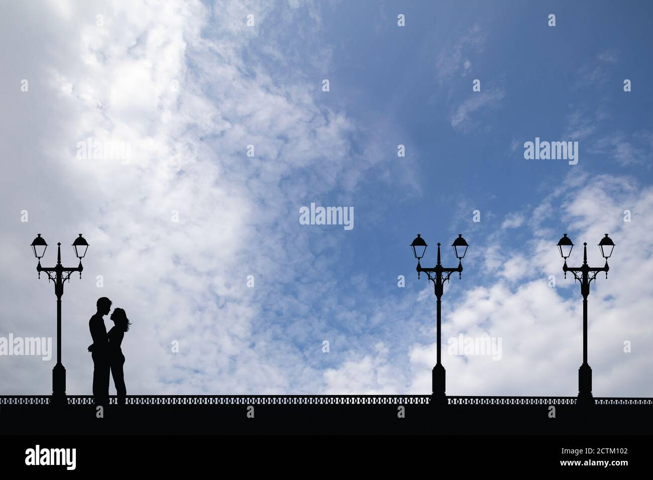 Silhouetten junger Liebhaber auf einer Promenade, die sich gegen einen blauen, wolkigen Himmel erstreckt Stockfoto