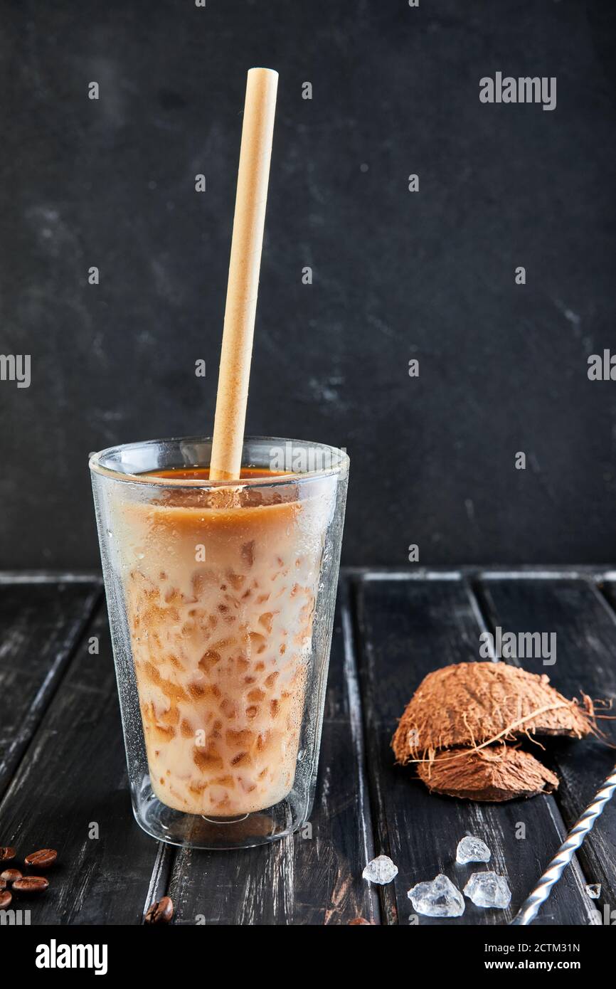Eiskaffee im Thai-Stil mit Kokosmilch und Kaffeebohnen auf schwarzem Holzhintergrund. Stockfoto