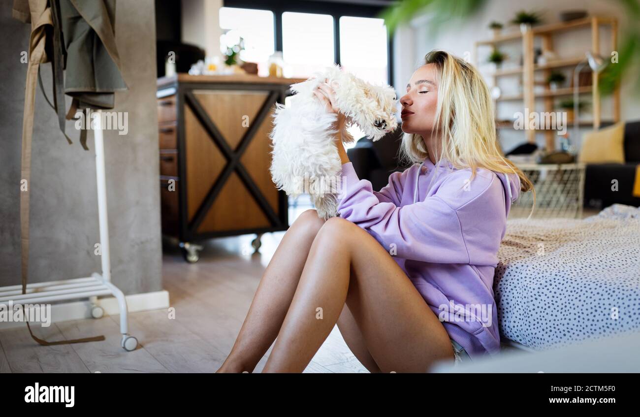 Schöne junge blonde Frau spielt mit ihrem Hund zu Hause, lächelnd Stockfoto