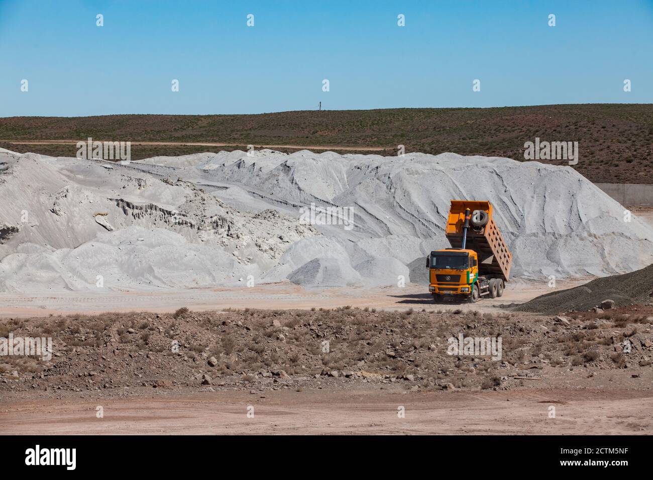 Mynaral/Kasachstan - April 23 2012: Blocklagerung von Rohstoffen in der Zementanlage von Jambyl. Mineralienhaufen (Klinker) und gelber Kipper. Stockfoto
