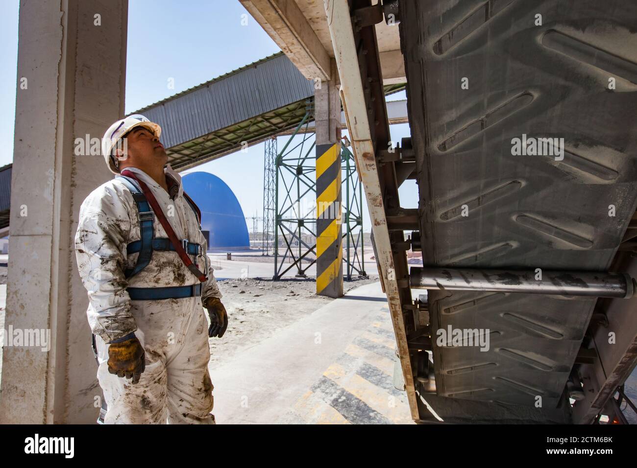 Kernkraftwerk von Jambyl. Ingenieur oder Wartungstechniker in weißem Helm und weißem schmutzigen Schutzanzug mit Gummiförderband auf industriellem Hintergrund Stockfoto