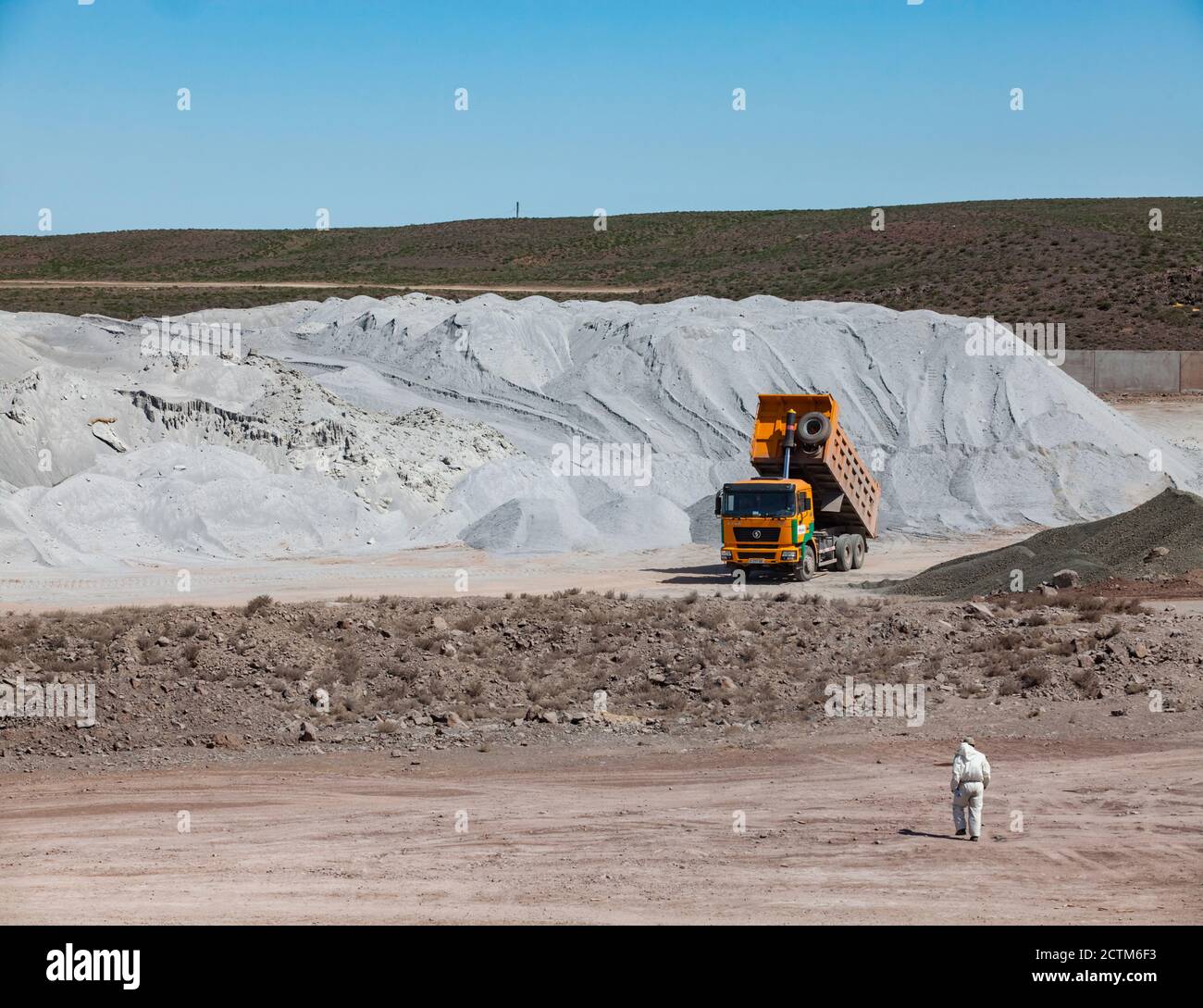 Lagerung von Rohstoffen in der Zementanlage von Jambyl. Haufen von Mineralien (Klinker) und Kipper und Arbeiter in weißen Schutzanzug. Stockfoto
