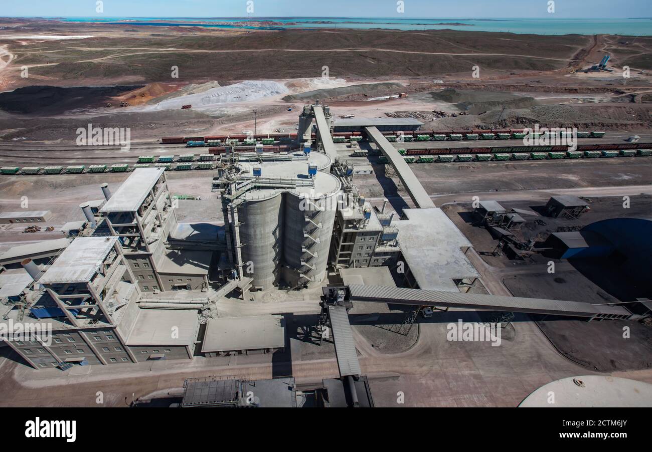 Mynaral, Kasachstan: Zementfabrik von Jambyl (Fabrik) . Luftaufnahme auf Silos und Bahnterminal mit Güterzug. See Balkhash am Horizont. Stockfoto
