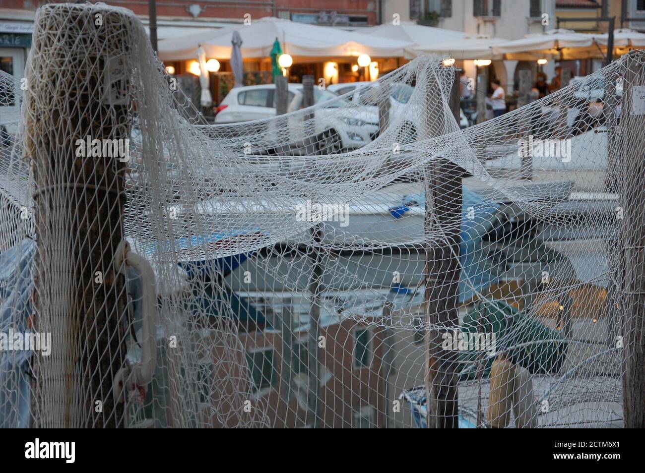 Das Fischnetz, das auf einigen hölzernen Pfosten in a trocknet kanal von Chioggia in der Lagune von Venedig mit Booten Und Straßenabendbeleuchtung im Hintergrund Stockfoto