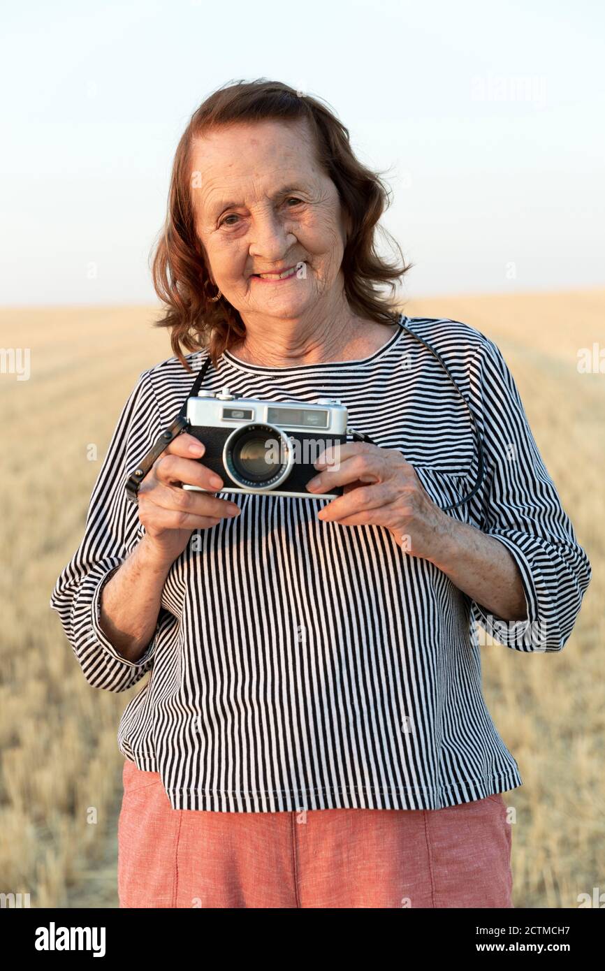 Porträt einer älteren Frau mit einer analogen Kamera auf dem Feld. Stockfoto