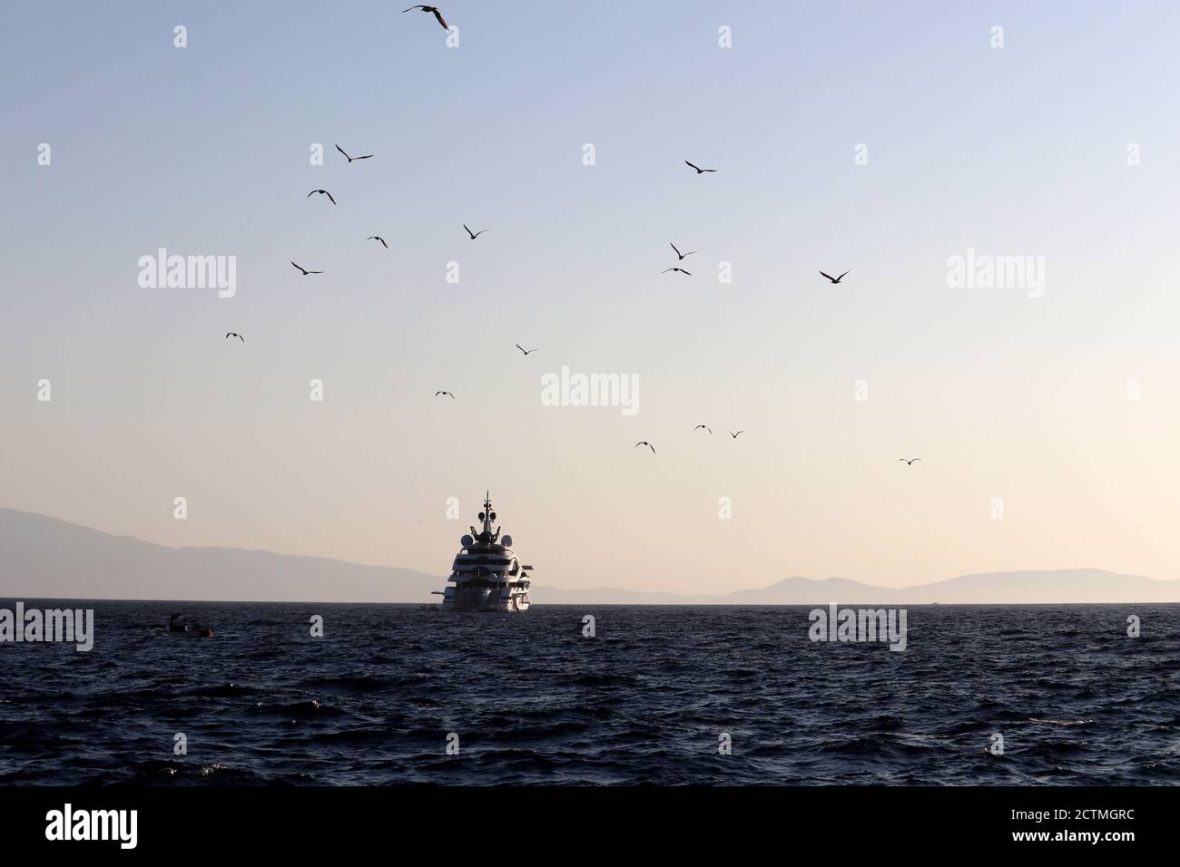 Malerische Seeslandschaft mit Luxusyacht und fliegenden Möwen Silhouetten auf nebligen Bergen Hintergrund. Landschaftlich schöner Blick auf das Abendmeer und die Inseln Stockfoto