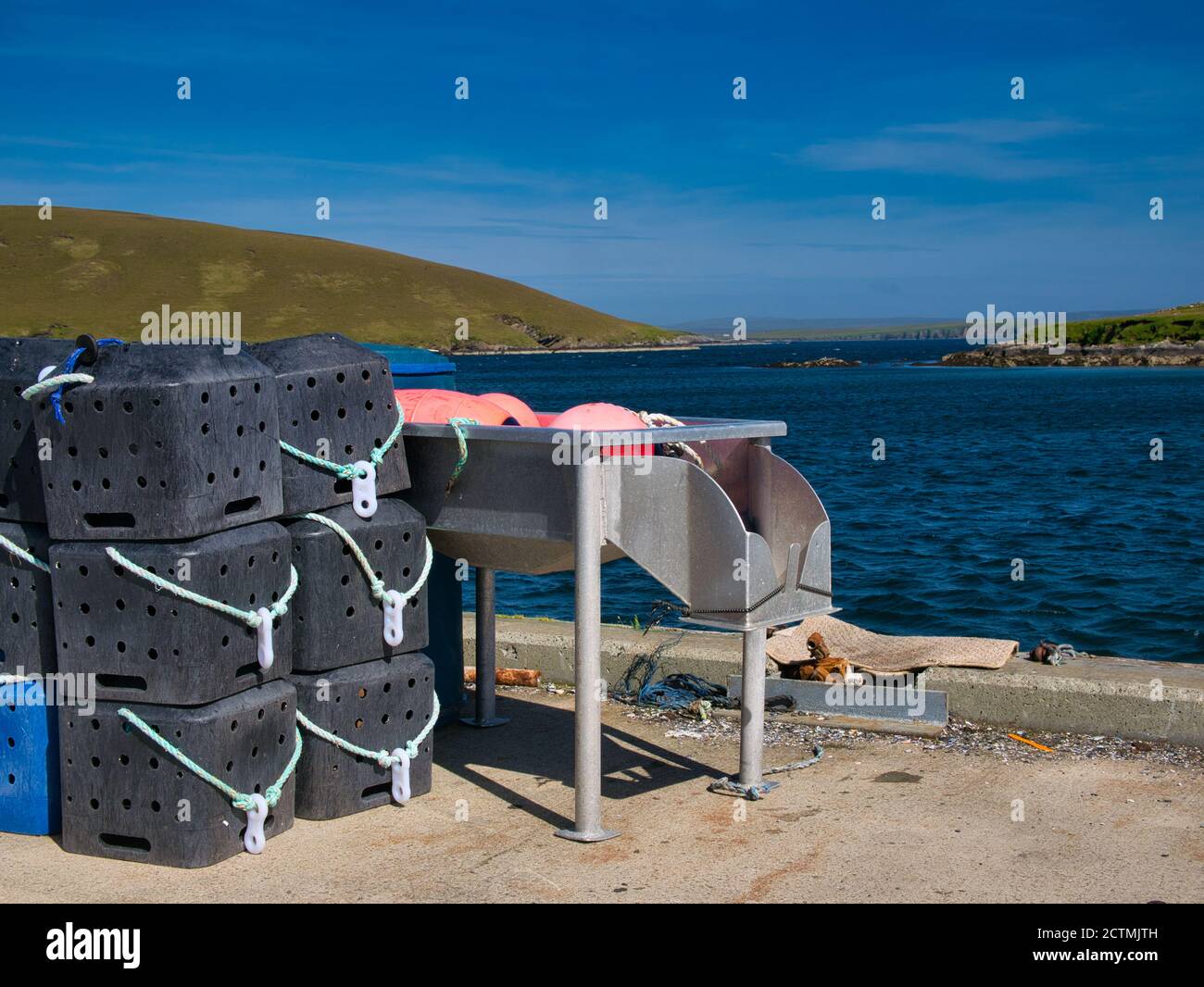 An einem sonnigen Sommertag stapelten sich schwarze Hummer-Töpfe aus Plastik auf einem Pier, der sofort benutzt werden kann, neben einem Fischausguß - aufgenommen in Shetland, Schottland, Großbritannien Stockfoto