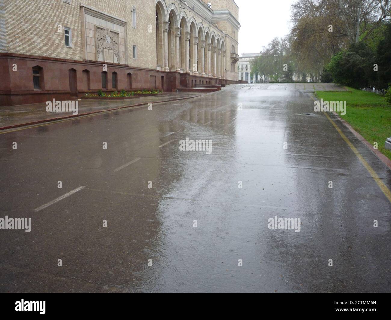 Straße bei regnerischem Wetter in der Nähe eines schönen architektonischen Gebäudes. Es regnet. Nasser Asphalt, Wasser läuft den Asphalt hinunter Stockfoto