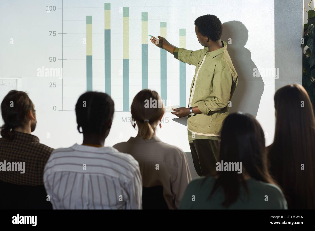 Porträt eines jungen afroamerikanischen Mannes, der auf Datengraph zeigt, während er während einer Geschäftskonferenz Rede hält oder über Statistiken berichtet, Raum kopieren Stockfoto