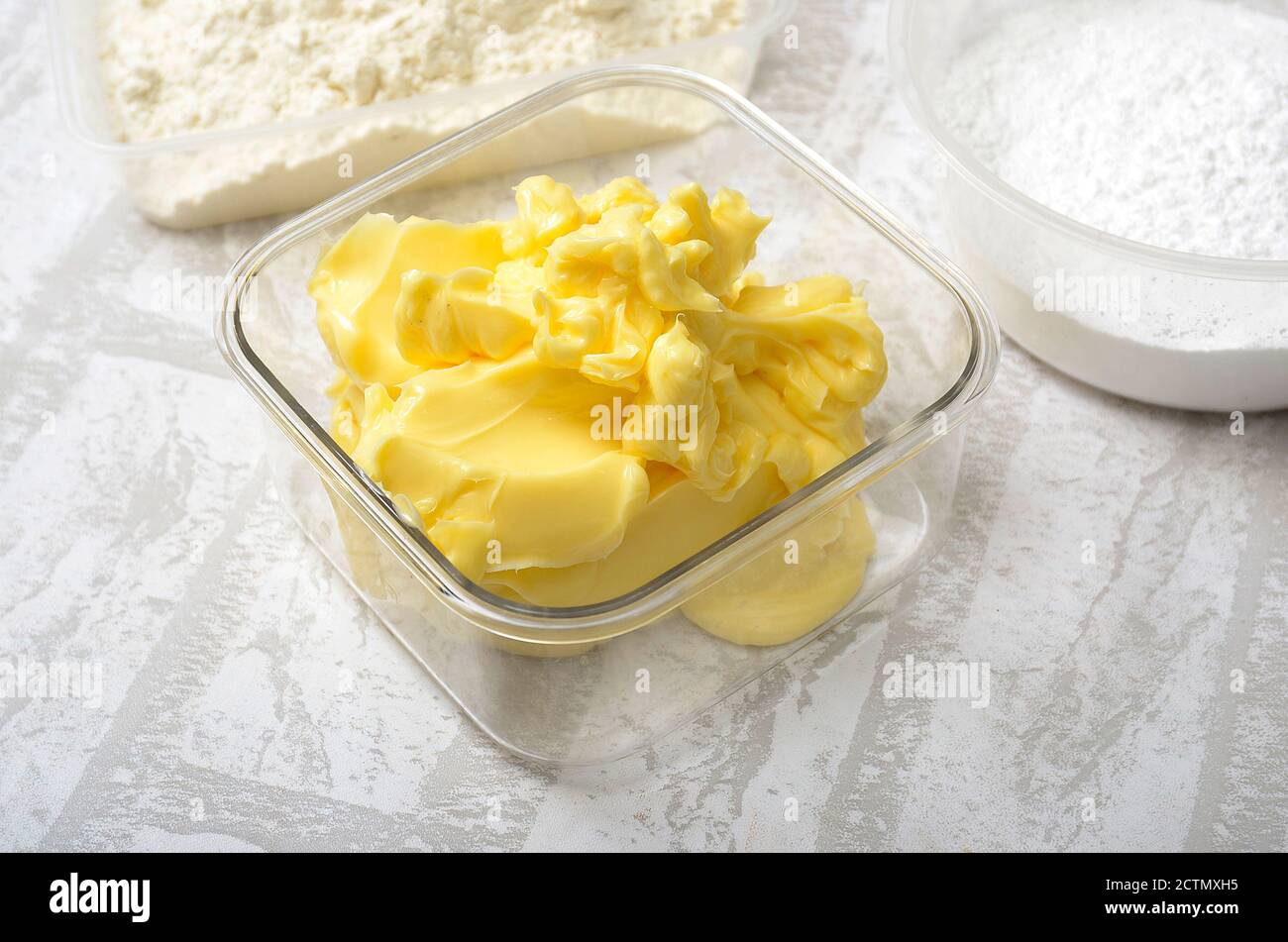 200 Gramm Butter in durchsichtiger Kunststoffschale. Butter zur Zubereitung von Keksen und Kuchen. Mit Backmehl und Zucker Stockfoto