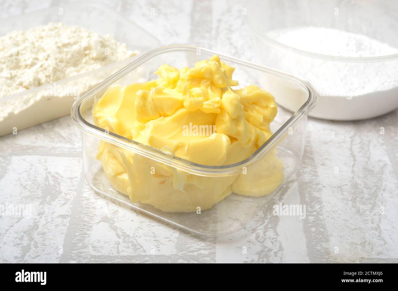 200 Gramm Butter in durchsichtiger Kunststoffschale. Butter zur Zubereitung von Keksen und Kuchen. Mit Backmehl und Zucker Stockfoto