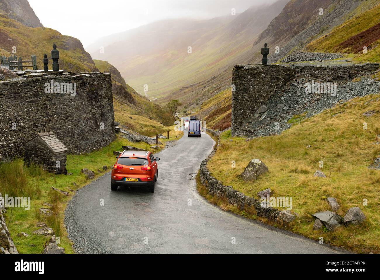 Honister Pass Summit - malerische Bergpassstraße im Lake District, England - Autos vorbei an Skulpturen auf beiden Seiten der Straße bei Honister Slate Mine Stockfoto