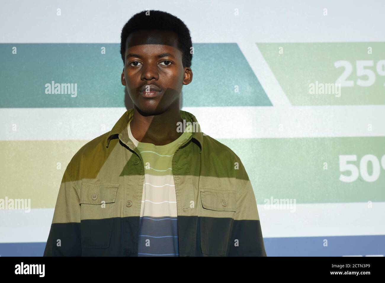 Waist-up-Porträt des jungen afroamerikanischen Mann stehen neben Projektor-Leinwand mit Streifen und Zahlen darauf, kopieren Raum Stockfoto