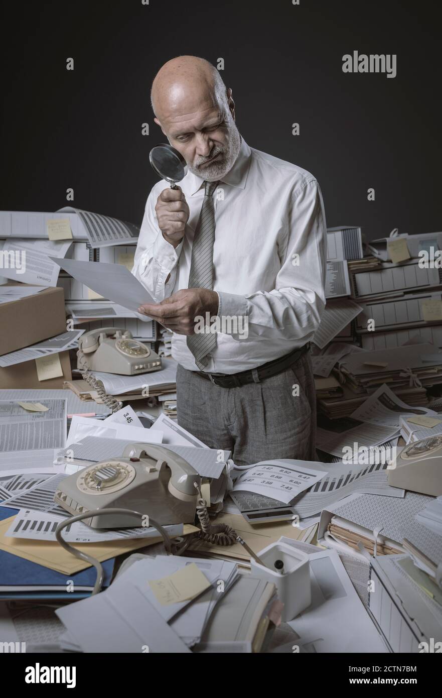 Ineffizienter Geschäftsmann mit Papierkram überladen, prüft er ein Dokument mit einer Lupe Stockfoto
