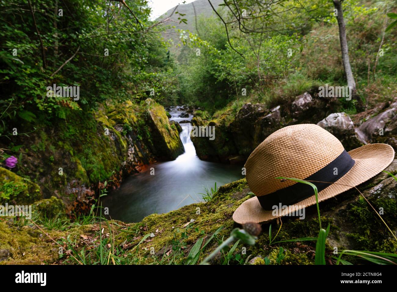 Stilvolle Strohhut auf moosigen Boden auf dem Hintergrund platziert Fluss in den Bergen in Langzeitbelichtung Stockfoto