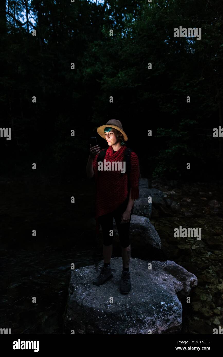 Weibliche Touristen stehen auf Felsen in Wäldern bei Nacht und Suche nach Route bei Verwendung der digitalen Karte auf dem Mobiltelefon Stockfoto