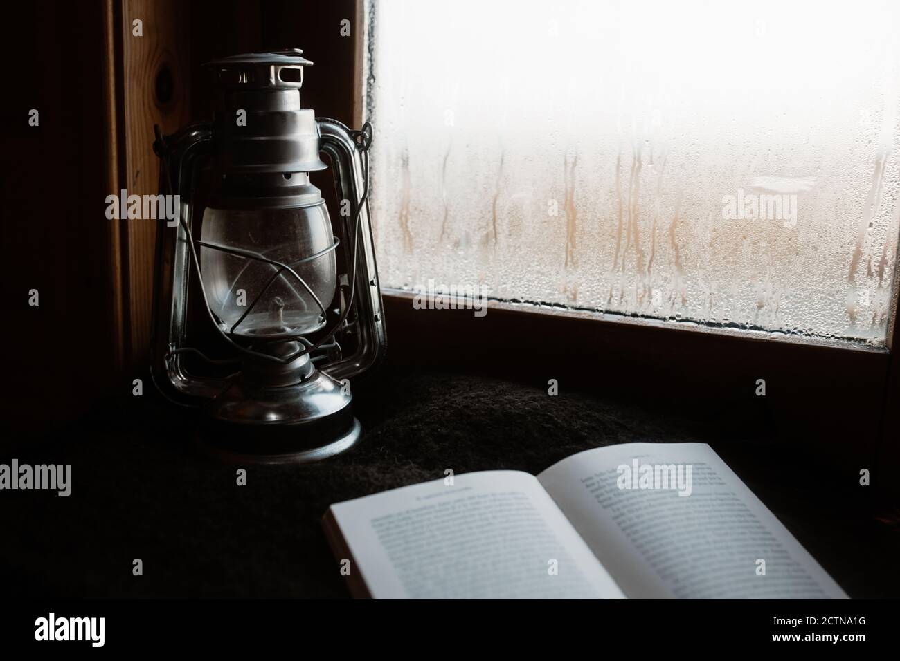 Gemütliche Atmosphäre der Zimmer mit Retro-Öl Laterne und geöffnet Buch auf Fensterbank mit Nebelfenster im Haus platziert Stockfoto