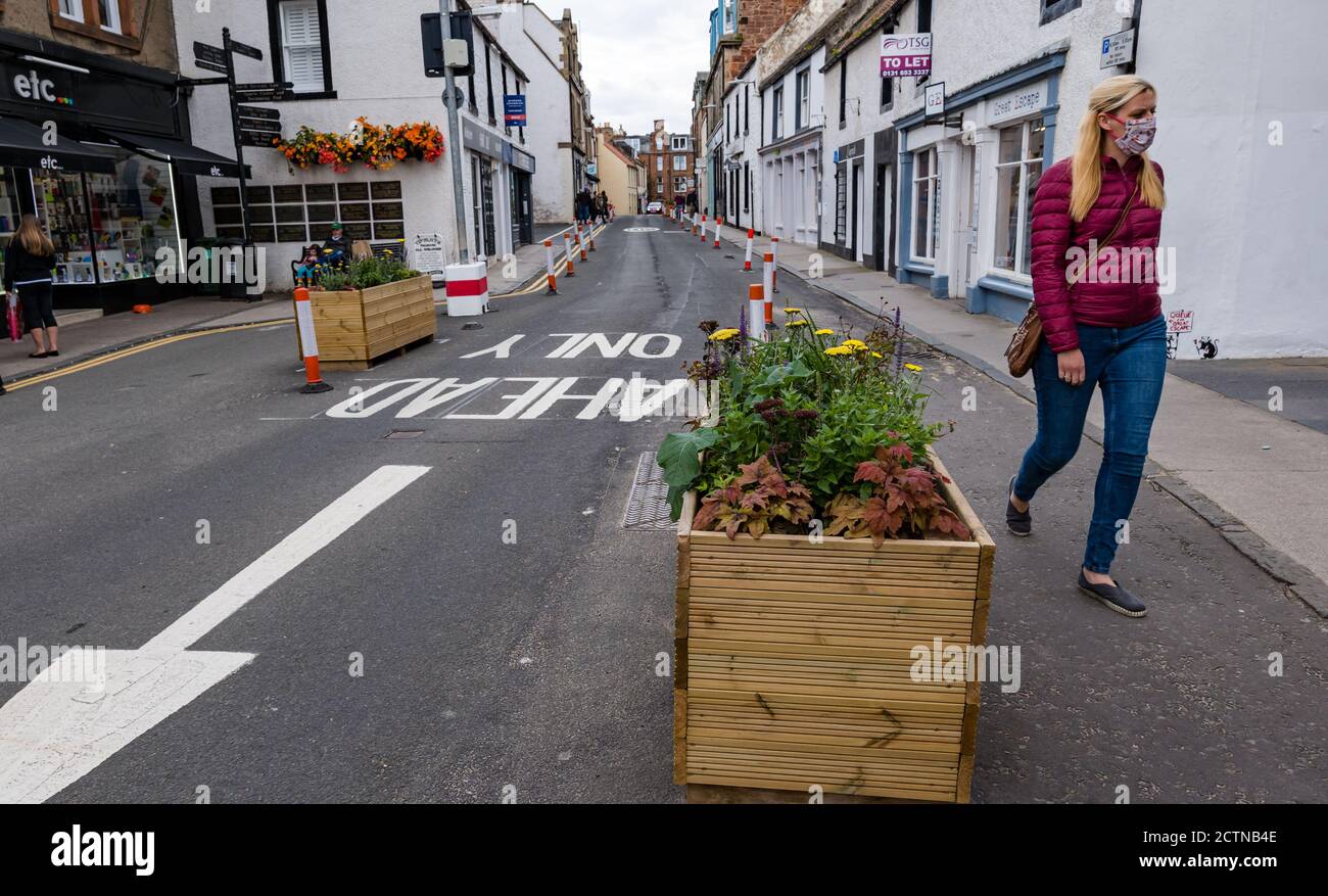 North Berwick, East Lothian, Schottland, Großbritannien, 24. September 2020. Die Covid-19 Coronavirus Pandemie Pflaster Verbreiterung Maßnahmen mit Straßenrand und Blumentöpfe in der engen High Street ermöglichen Fußgängern mehr Platz als eine Frau trägt eine Gesichtsmaske Spaziergänge entlang der Straße Stockfoto