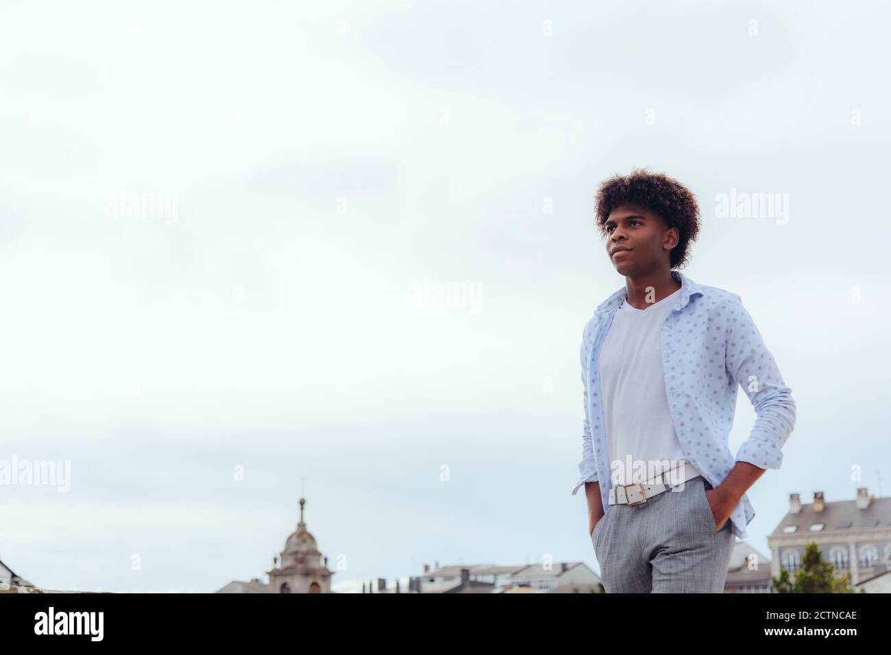 Stilvoller schwarzer Rüde mit Afro-Frisur, der mit den Händen läuft Taschen auf der Straße und lächelnd e Blick weg Stockfoto