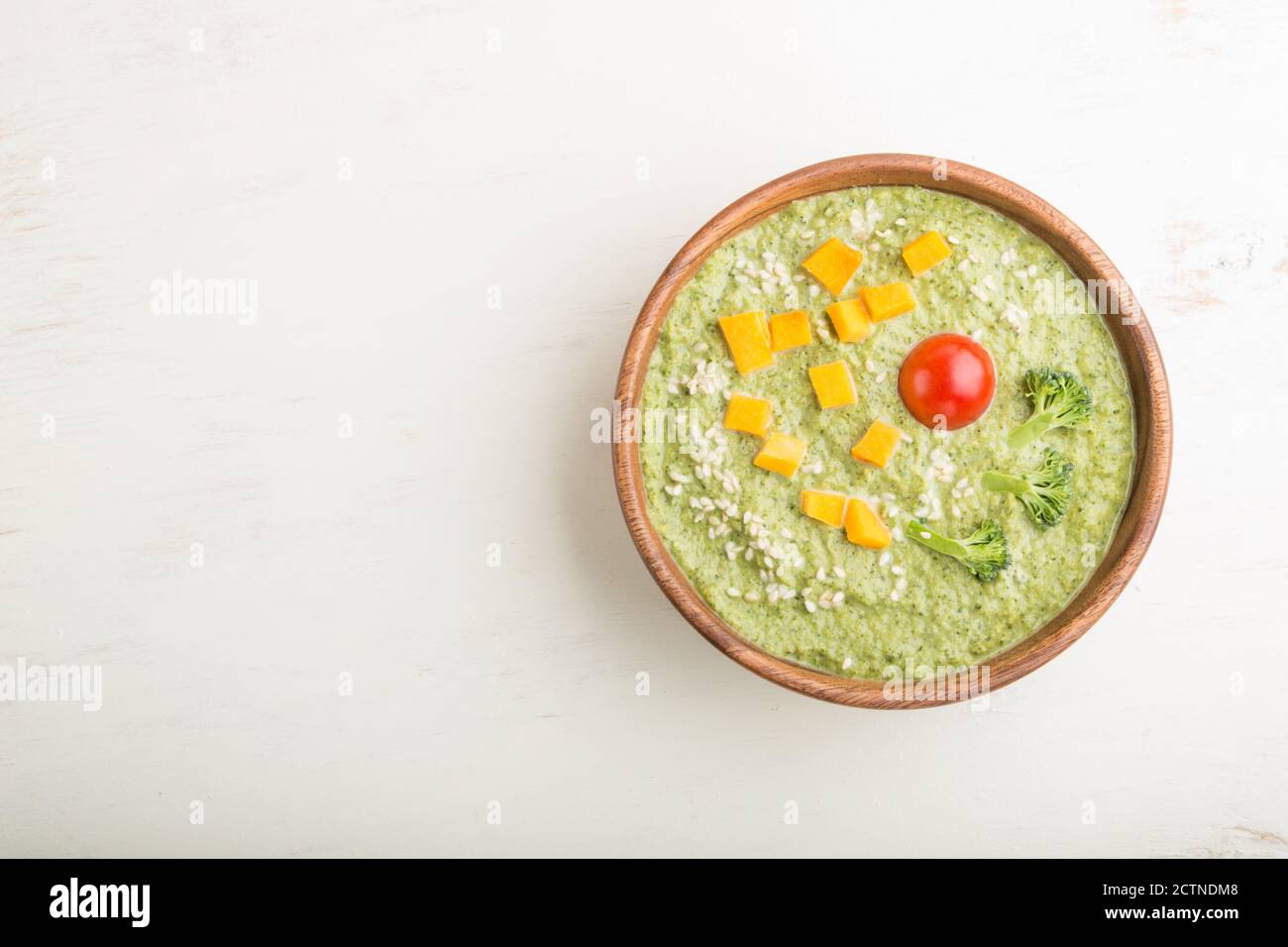 Grüne Brokkoli-Cremesuppe in Holzschüssel auf weißem Holzhintergrund. Draufsicht, flaches Lay, Kopierraum. Stockfoto