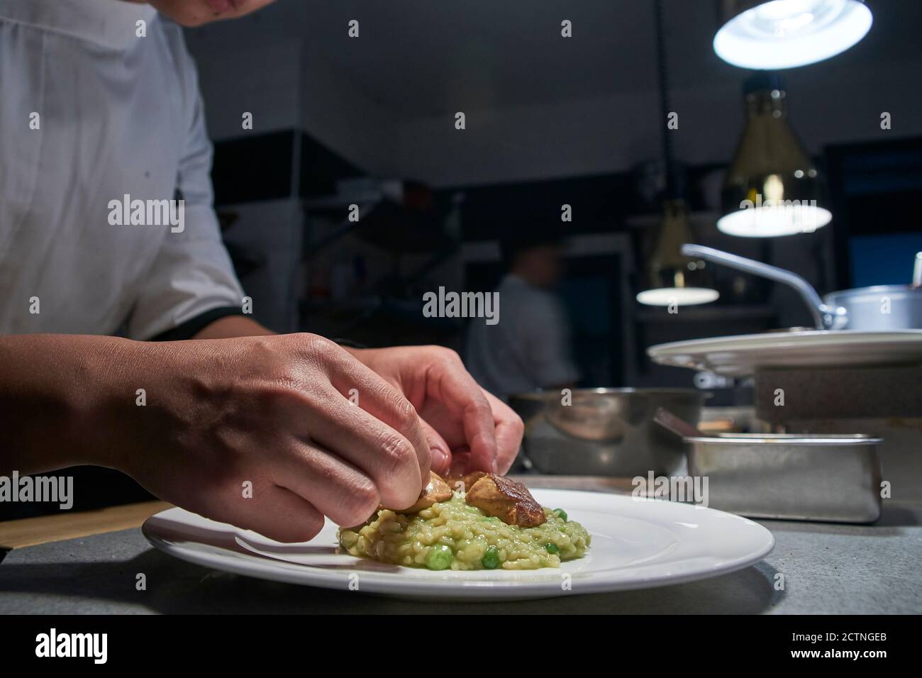 Seitenansicht des Ernteguts unkenntlich Koch Montage Fleischstücke Auf eine Portion leckeres Risotto während der Zubereitung der Bestellung in zeitgenössischem Restaurant Küche Stockfoto