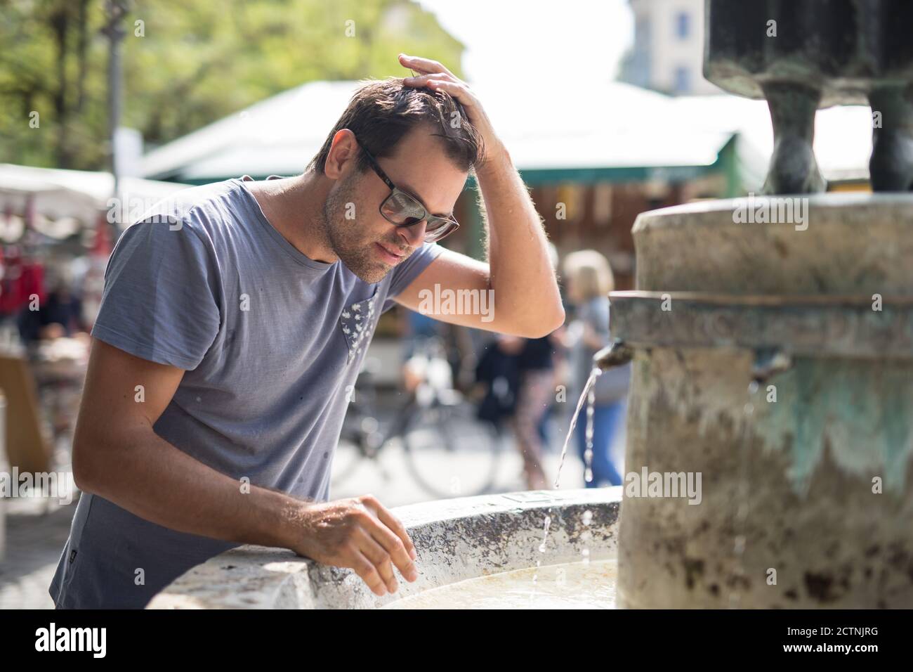 Junge Casual cucasian Mann erfrischt sich mit Wasser aus der Öffentlichkeit Stadtbrunnen an einem heißen Sommertag Stockfoto