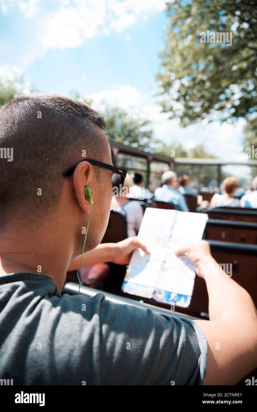 Nahaufnahme eines jungen Kakausenmanns, der in einem offenen Tourbus unterwegs ist, einen Stadtplan überprüft und Kopfhörer benutzt Stockfoto