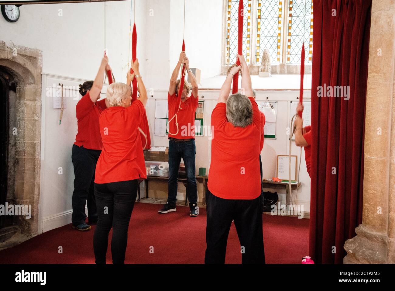 Eine Gruppe von Menschen in roten Spitzen läutete eine Kirchenglocke in Norfolk, Großbritannien Stockfoto