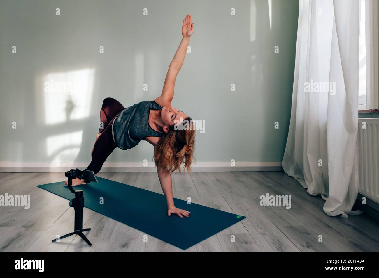 Weibliche Yoga-Lehrerin verbunden von zu Hause Blogging und vlogging Rundfunk Unterricht über soziale Medien mit Smartphone auf Gimbal Stockfoto