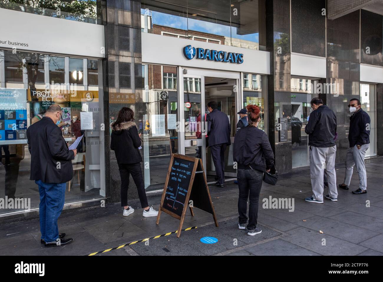 Fußgänger bilden eine Schlange vor einer Barclays Bank Filiale in der Edgware Road in London, während die Menschen den finanziellen Druck der Coronavirus-Pandemie spüren. Stockfoto