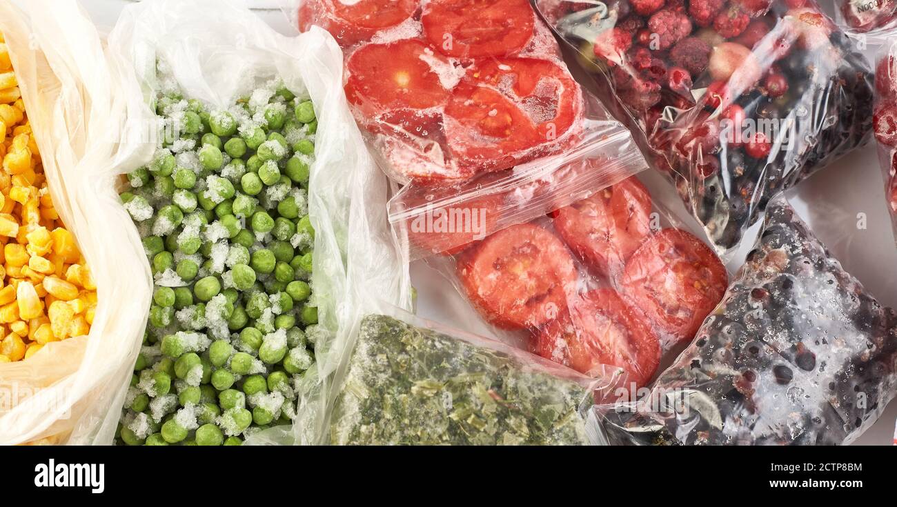 Eine Reihe von Tiefkühlkost für den Winter. Gefrorene Beeren, Gemüse, Mais, grüne Erbsen, Tomaten im Gefrierschrank. Stockfoto