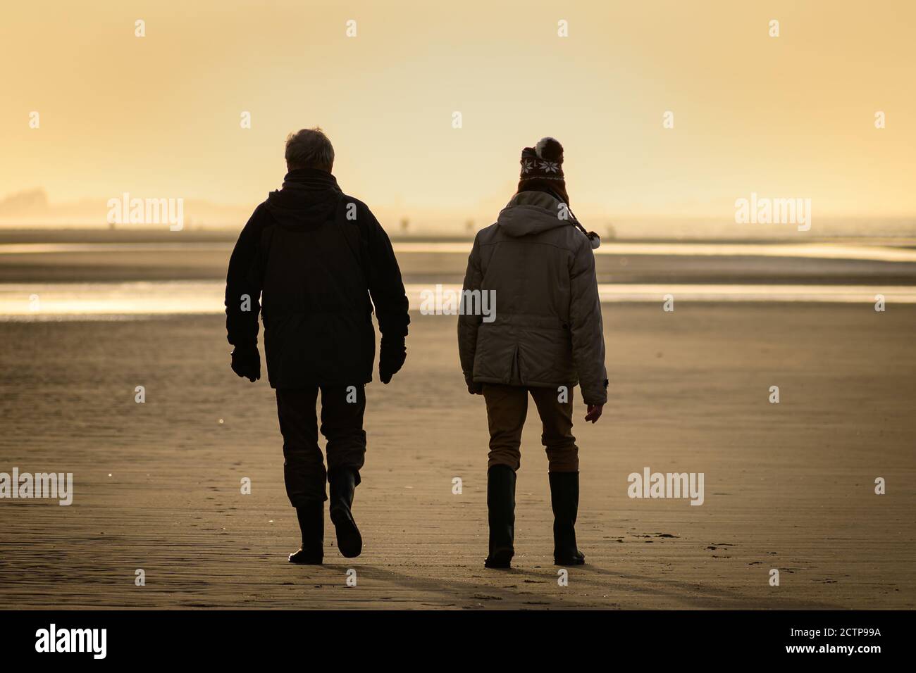 Zwei Männer, die bei Sonnenuntergang am Strand von der Rückseite aus gesehen wurden. Stockfoto