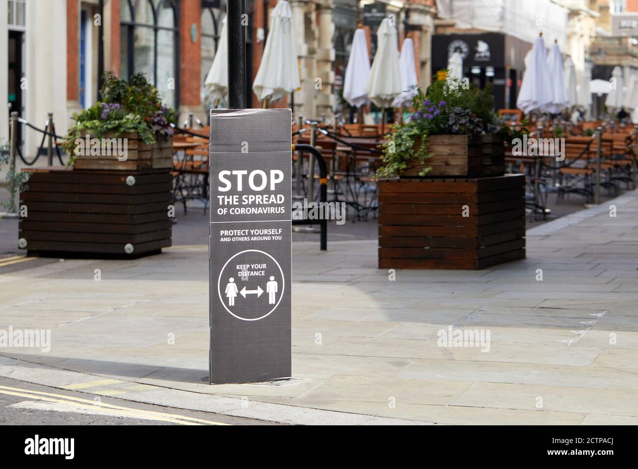 London, Großbritannien. - 21. September 2020: Ein Straßenschild - das Fußgänger zur sozialen Distanz auffordert - vor leeren Stühlen und Tischen im Freien eines Covent Garden Restaurants. Stockfoto
