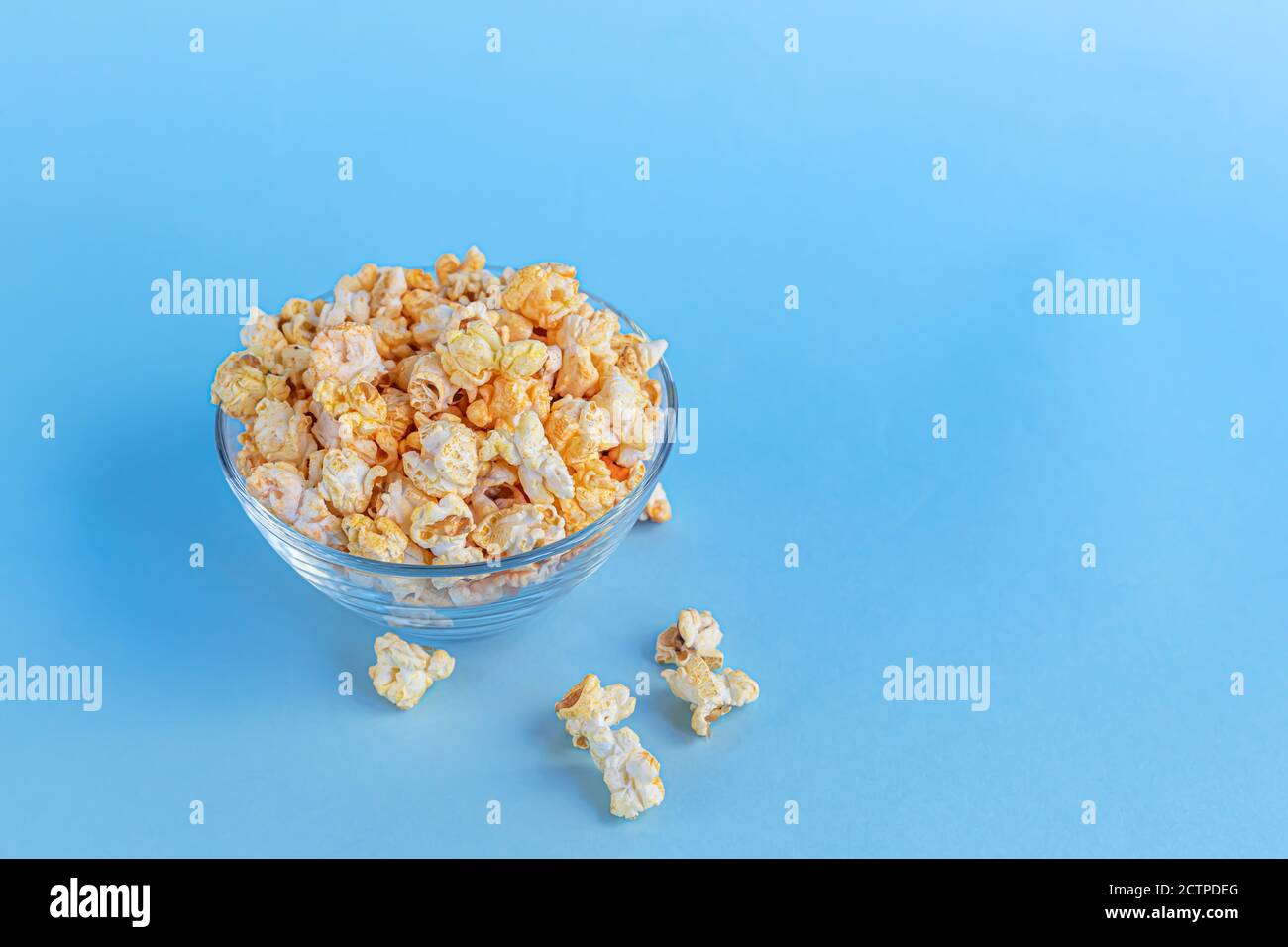 Eine transparente Schüssel Popcorn auf einer blauen Oberfläche. Heimfamilie beim Ansehen von Filmen. Speicherplatz kopieren. Stockfoto