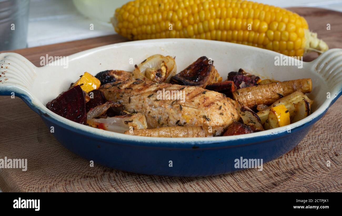 Ein gegrilltes Hähnchen sitzt auf einer Keramikplatte neben verschiedenen Wurzelgemüse. Verkohlte Linien aus dem Skillet-Muster sind deutlich sichtbar. Stockfoto