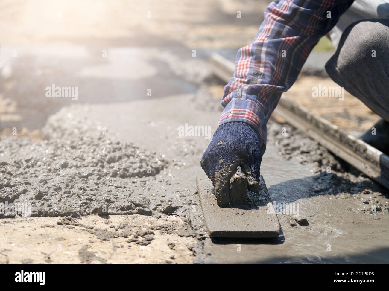 Nahaufnahme der Hände von Bauarbeitern mit Handschuhen und Kelle Überschüssiges Mischungsniveau mit Holz abkratzen bildet frisch gegossenen Beton Pad Stockfoto