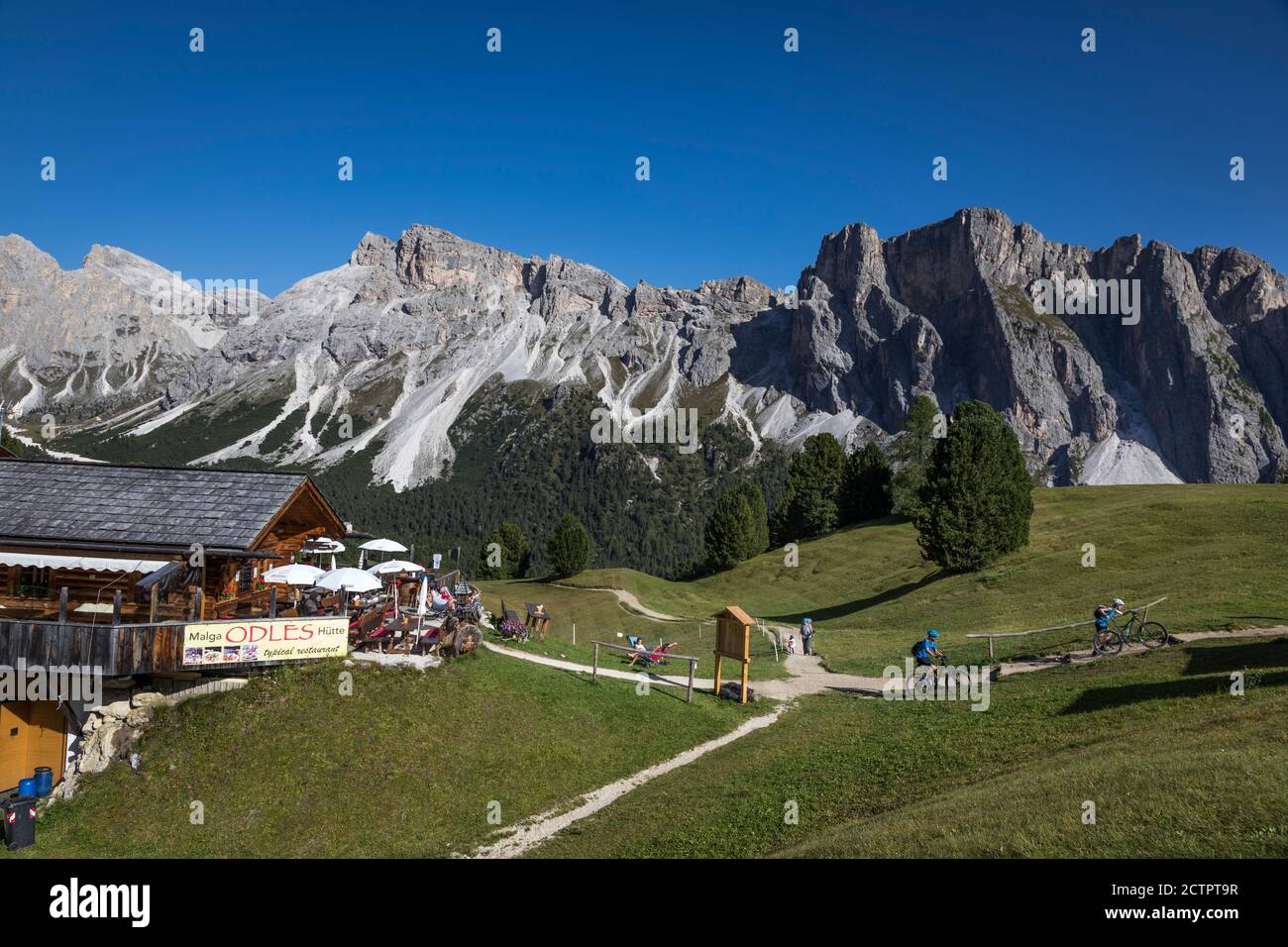 Radfahrer verlassen ein Bergrestaurant und gehen auf eine Bergstrecke mit spektakulärem Blick auf die Dolomiten rund um Gröden, Italien. Stockfoto