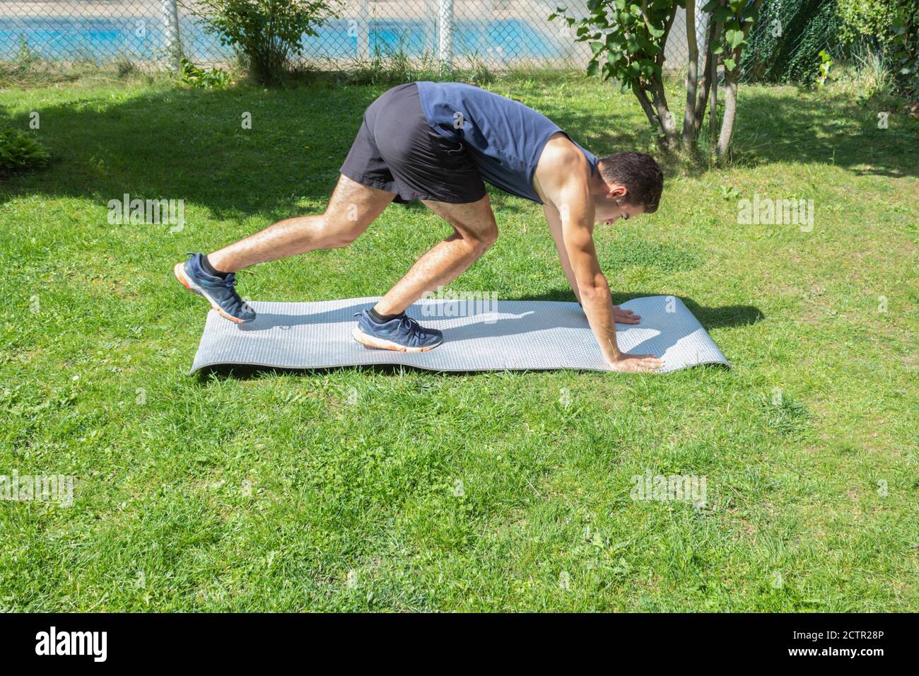 Junge in Fitness-Kleidung Biegen über, um fertig zu werden Mit einer Matte zum Aufwärmen und Trainieren von Routinen Der Garten eines Hauses an einem sonnigen Tag Stockfoto