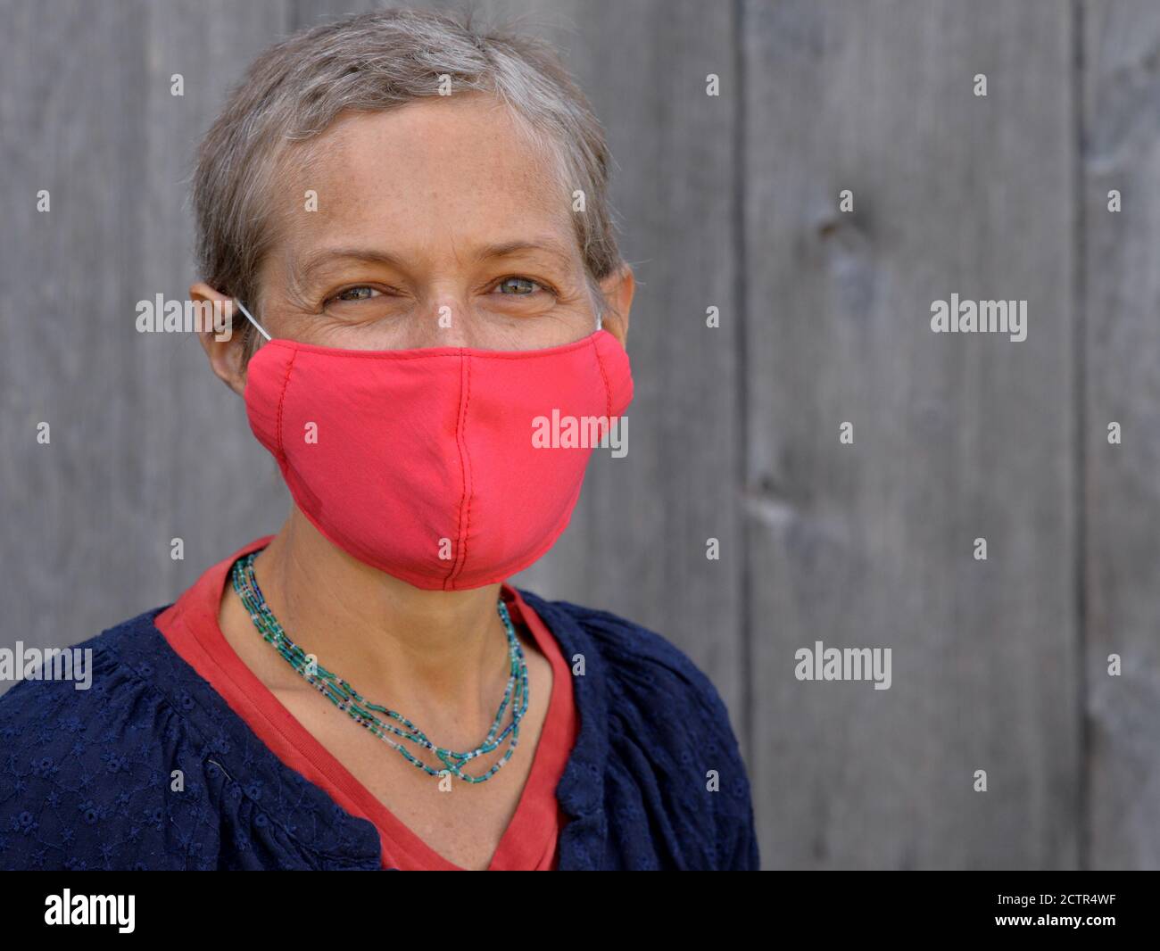 Eine kaukasische Frau mittleren Alters mit kurzen Haaren trägt während der Corona-Virus-Pandemie von 2019/20 eine rote, selbstgemachte, nicht-medizinische Gesichtsmaske. Stockfoto