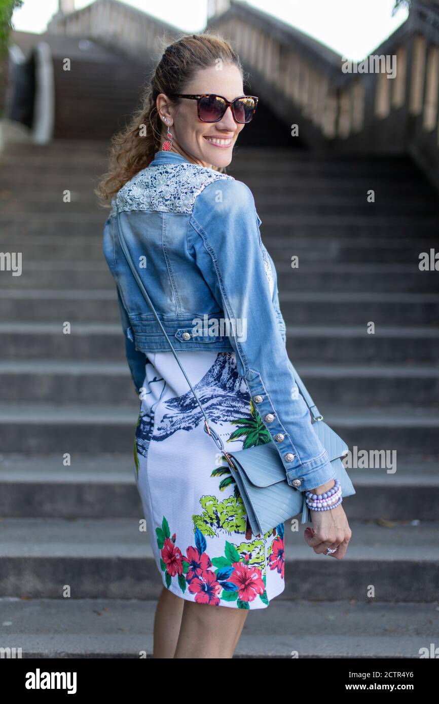 Glückliche junge kaukasische Stadtfrau in Sonnenbrille Blick zurück auf Treppen im Park, toothy Lächeln Stockfoto