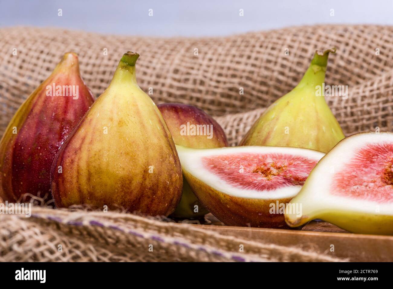 Frische Feigen in zwei Hälften geschnitten mit ganzen Feigen im Hintergrund, auf einer hölzernen Oberfläche. Feigen Sie die Früchte auf einer hölzernen Platte. Stockfoto