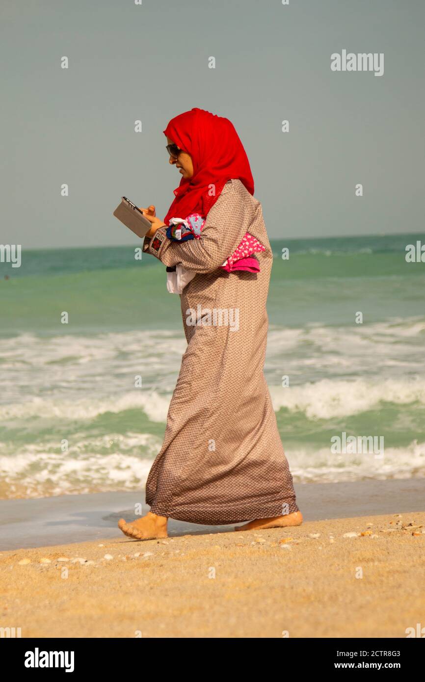 Eine arabische Frau, die am Persischen Golf mit ihrem Handy in der Nähe von Dubai, Vereinigte Arabische Emirate, unterwegs ist Stockfoto