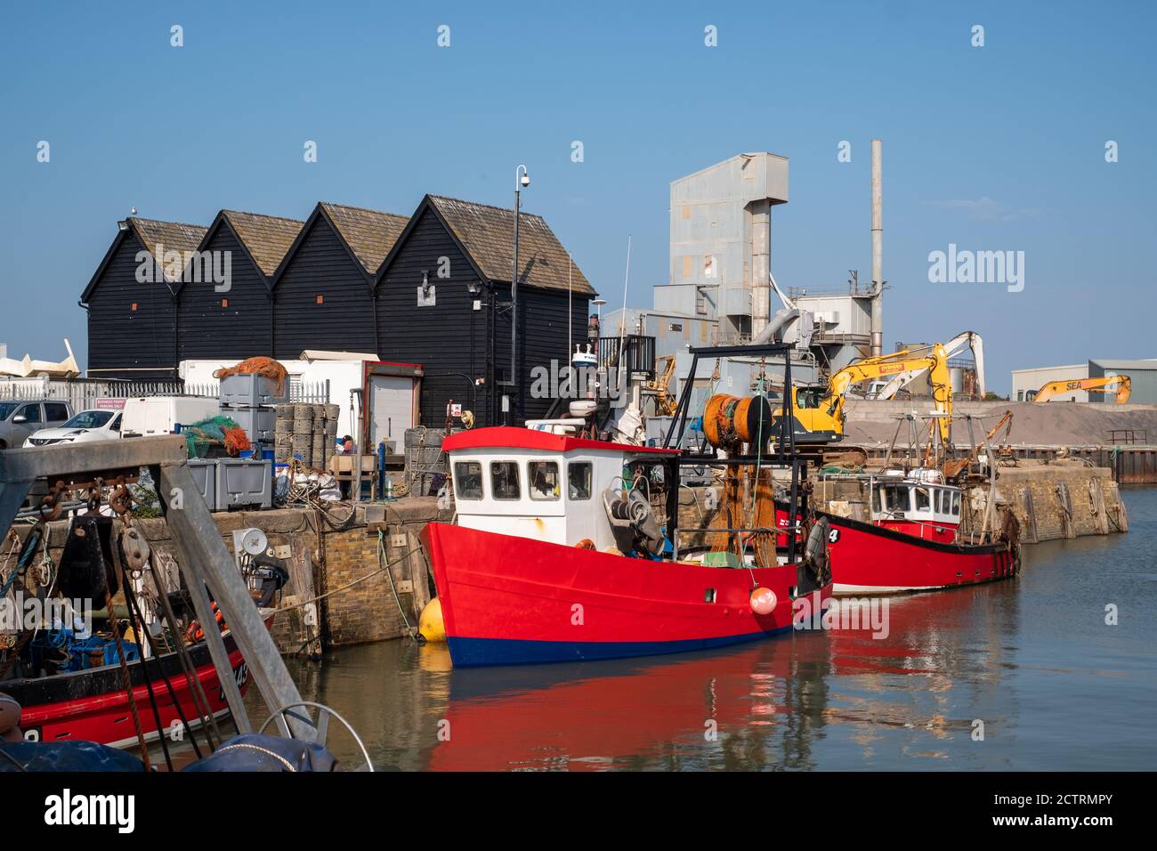Fischerboote im Dock vor schwarz lackierten Holzlagerhallen in Whistable, Kent, UK Stockfoto